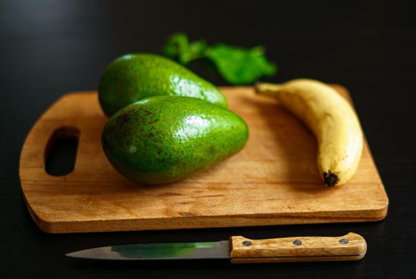 Šviežių vaisių ir daržovių asortimentas su bananais, špinatais ir avokadais ant medinio stalo