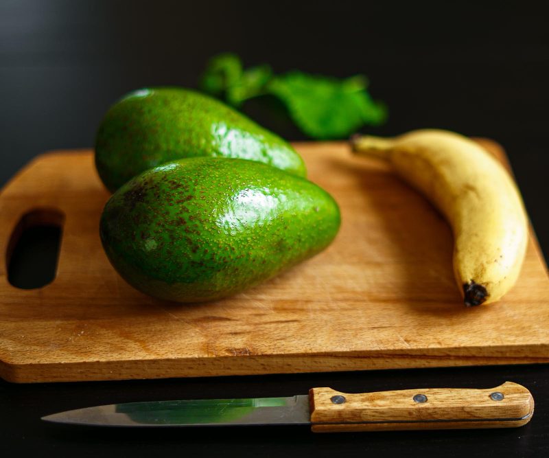 Šviežių vaisių ir daržovių asortimentas su bananais, špinatais ir avokadais ant medinio stalo